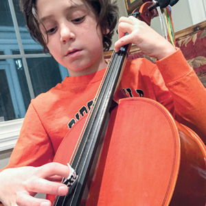 Photo of a kid playing the cello while using an invention of his to protect his fingers when playing
